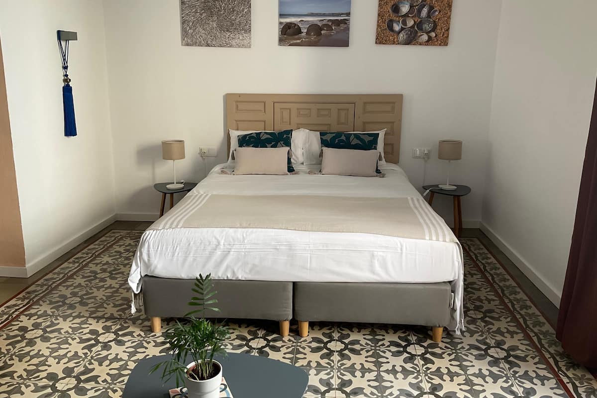 Una habitación de hotel ordenada con una cama grande, dos mesitas de noche, una planta en maceta y tres obras de arte colgadas en la pared.