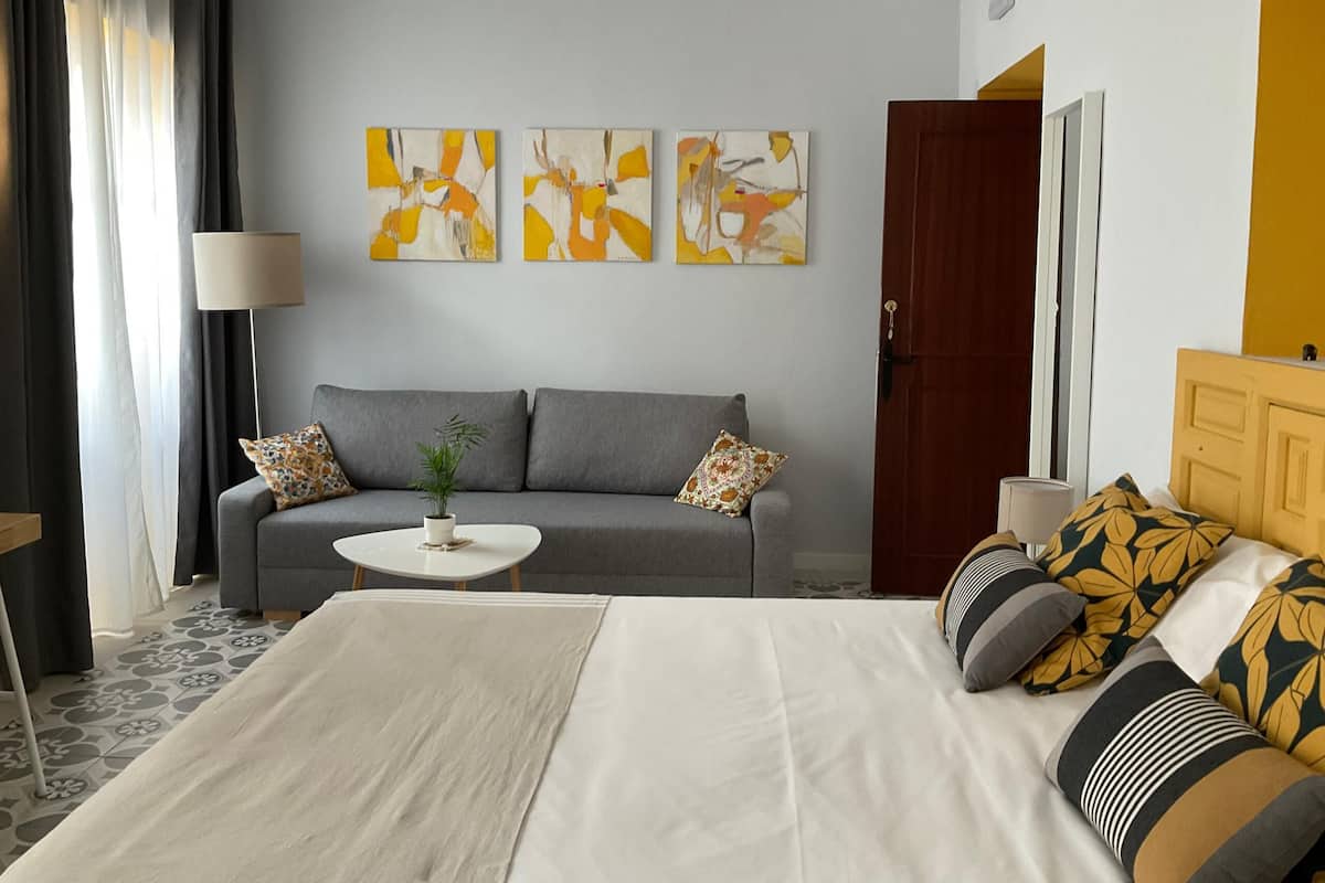 Una habitación de hotel moderna con un sofá gris, una cama blanca y arte abstracto en la pared.
