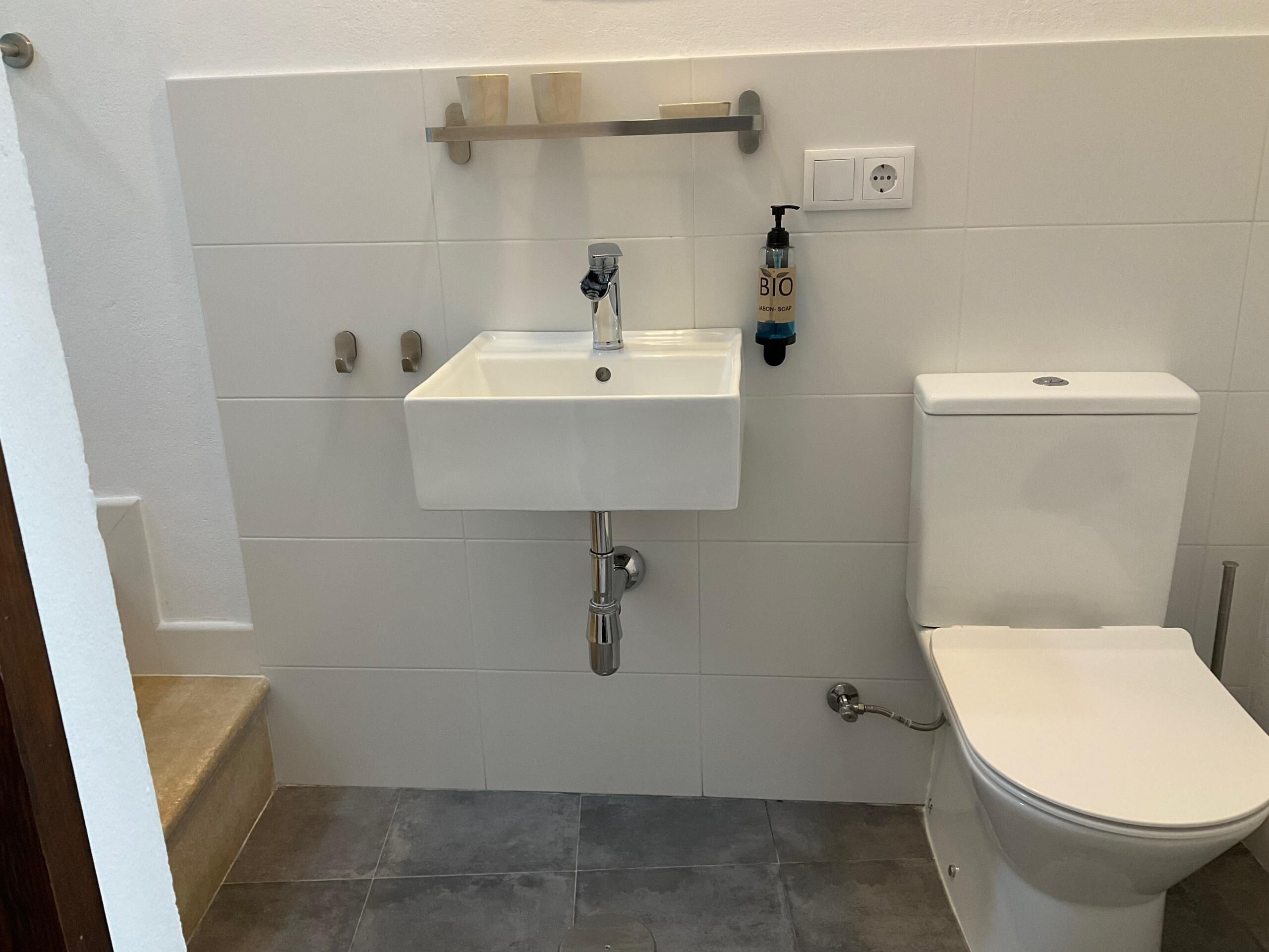 Une salle de bain avec un lavabo blanc, des toilettes et une étagère au-dessus du lavabo.
