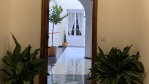 Un pasillo con una puerta de madera que da a un espacio exterior con plantas en macetas y vistas de un edificio blanco.