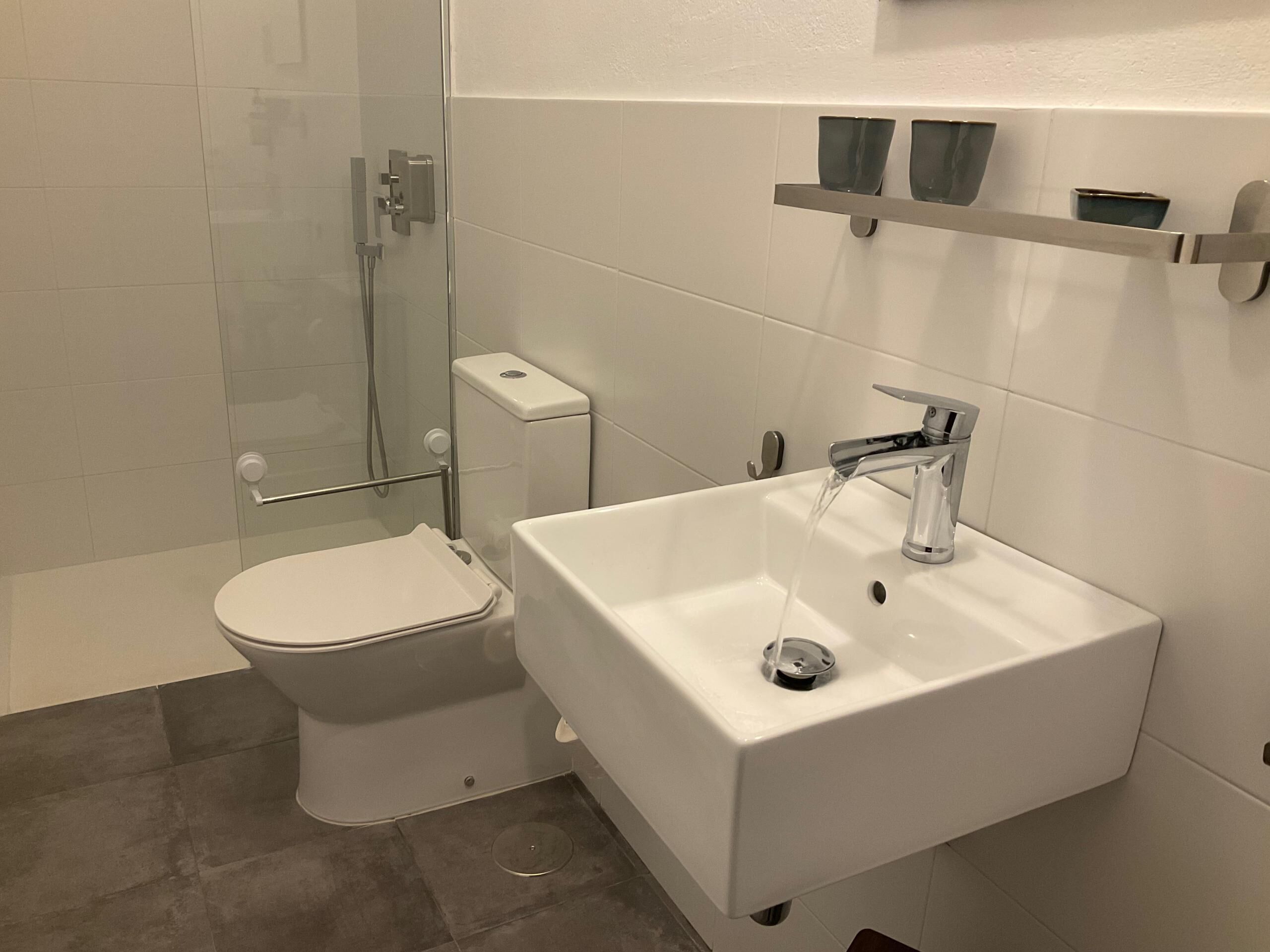 Een moderne badkamer met toilet, een douchecabine van glas en een wastafel met kraan.