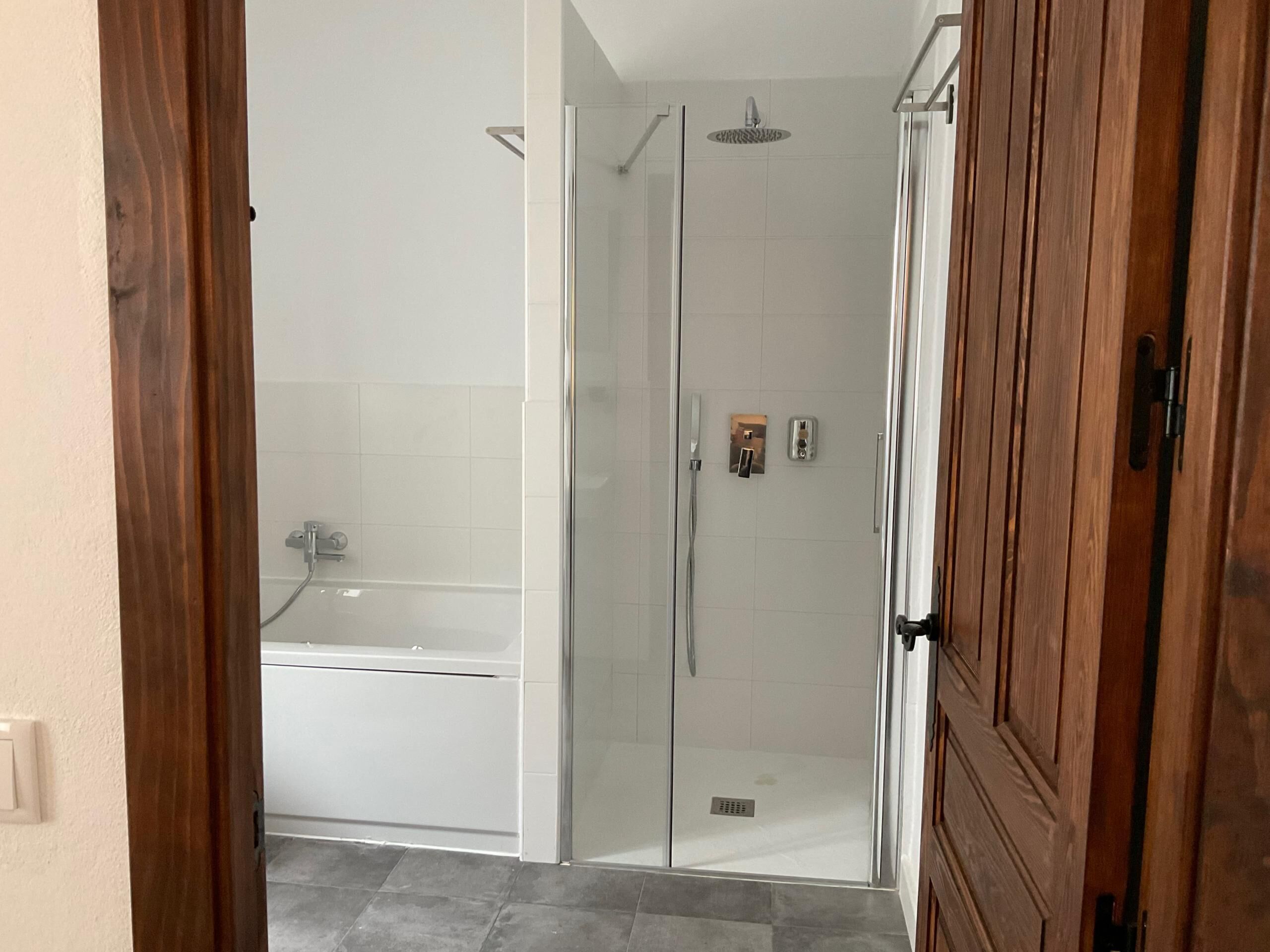 A bathroom with a glass-enclosed shower, a white bathtub, and a wooden door.