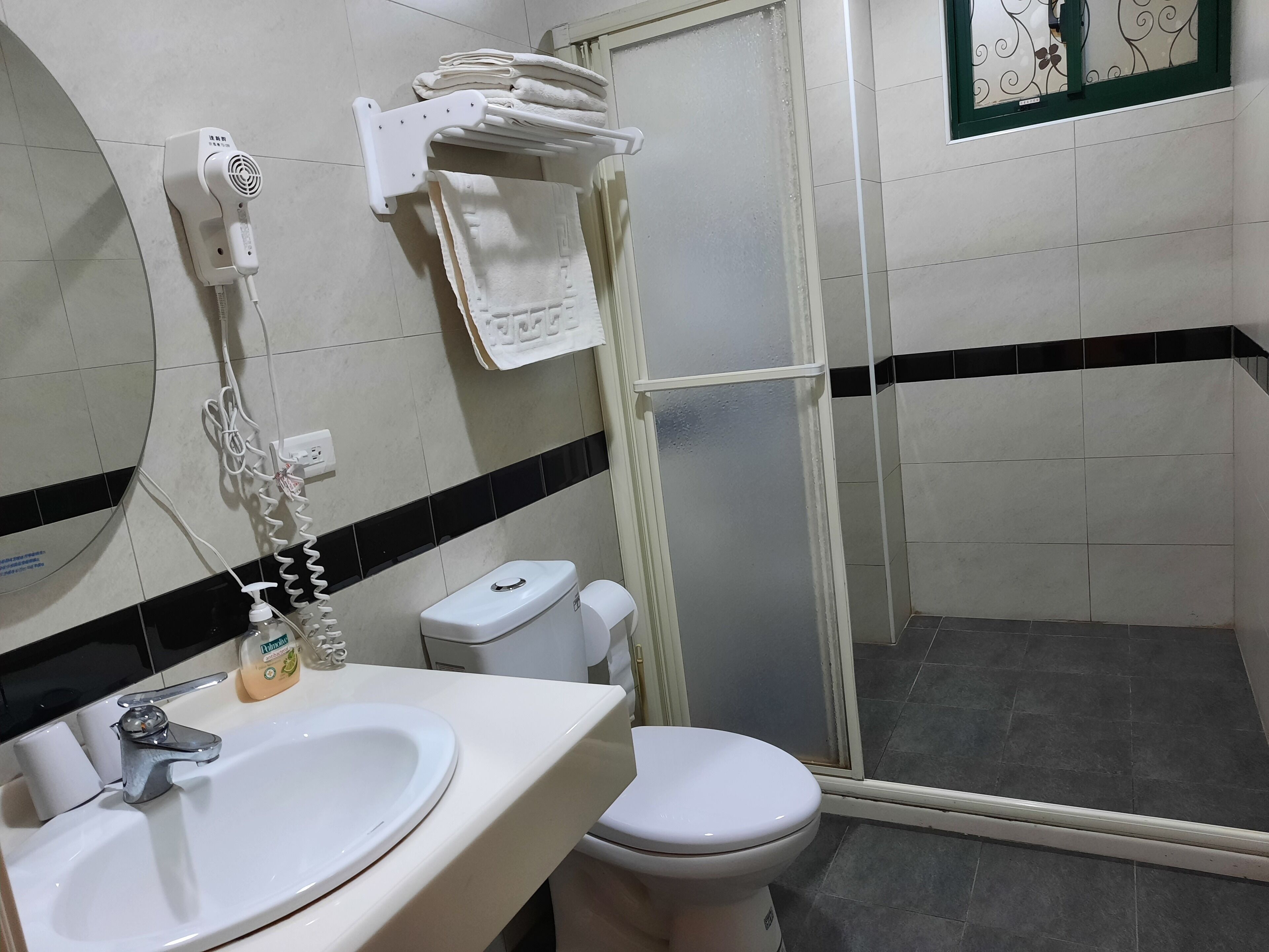 Un baño con un lavamanos blanco, un inodoro, una ducha con puerta de vidrio y un perchero con toallas dobladas.