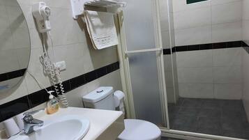 Un baño con un lavamanos blanco, un inodoro, una ducha con puerta de vidrio y un perchero con toallas dobladas.