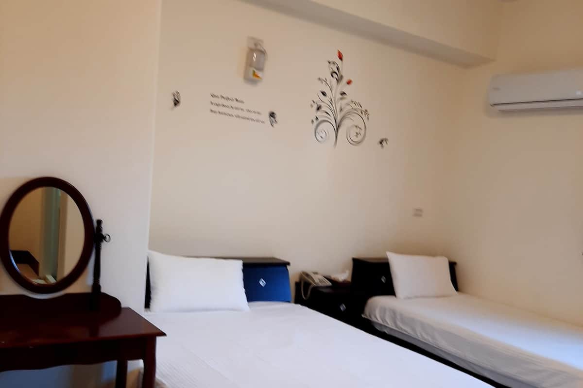 Een hotelkamer met twee eenpersoonsbedden, een houten bureau met stoel, een spiegel en een wandairconditioner.