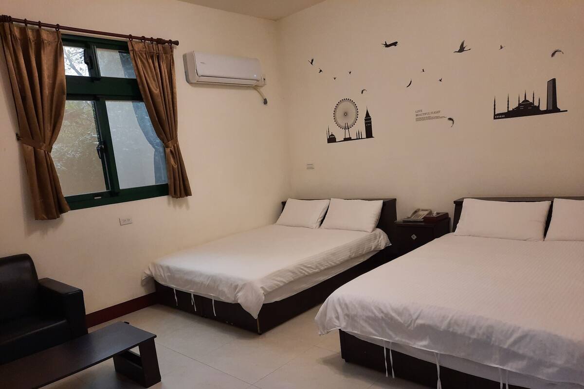 Een hotelkamer met twee eenpersoonsbedden, een bureau, een stoel en een raam met gordijnen.