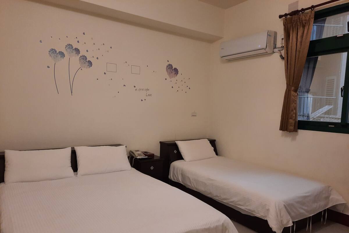 Een kamer met twee bedden, een wandairconditioner en een raam met gordijnen.