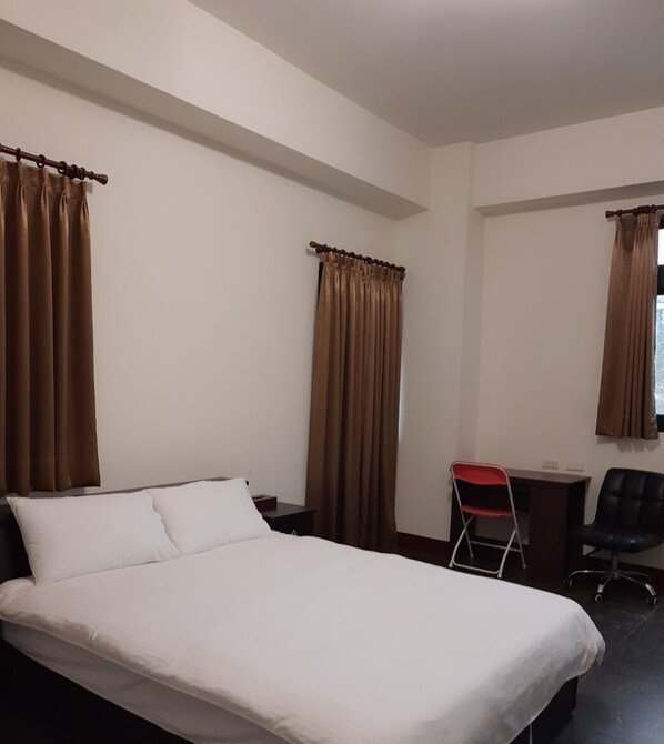 A hotel room with a single bed, a desk, a chair, and two windows with curtains.