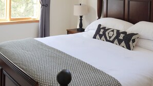 Una camera da letto con un letto grande, una testiera in legno, un comodino con una lampada, una finestra con tende e vista sugli alberi.