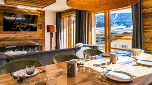 A dining area with a wooden table set for four, a large black pendant light, and a TV mounted on the wall displaying "Inmo Select". - Cozy duplex, 8 ppl, parking, Les Gets (Les Gets)
