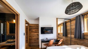 A modern hotel room with a wooden floor, a bed with white linens, a desk with a chair, a television, and a large mirror. - Cozy duplex, 8 ppl, parking, Les Gets (Les Gets)