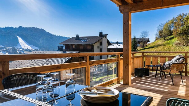 A wooden deck with a table set for dining, overlooking a mountainous landscape with a ski slope. - Cozy duplex, 8 ppl, parking, Les Gets (Les Gets)