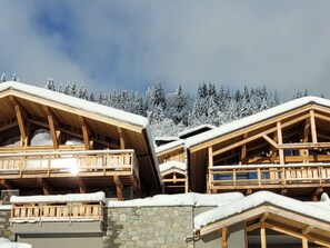 A wooden chalet with a stone foundation, multiple balconies, and a view of snow-covered trees.