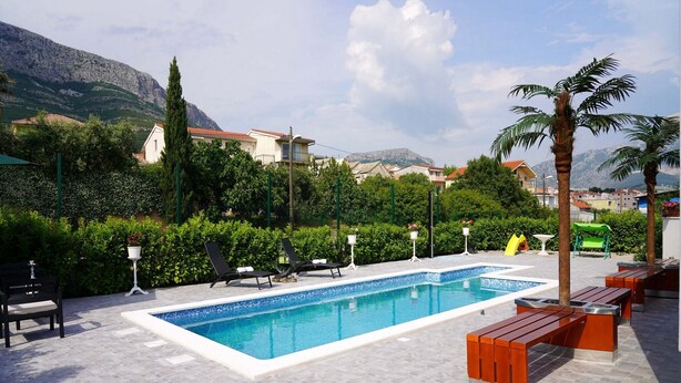 A swimming pool with lounge chairs and a wooden bench, surrounded by greenery and mountains in the background. - Villa Daniela (Solin)