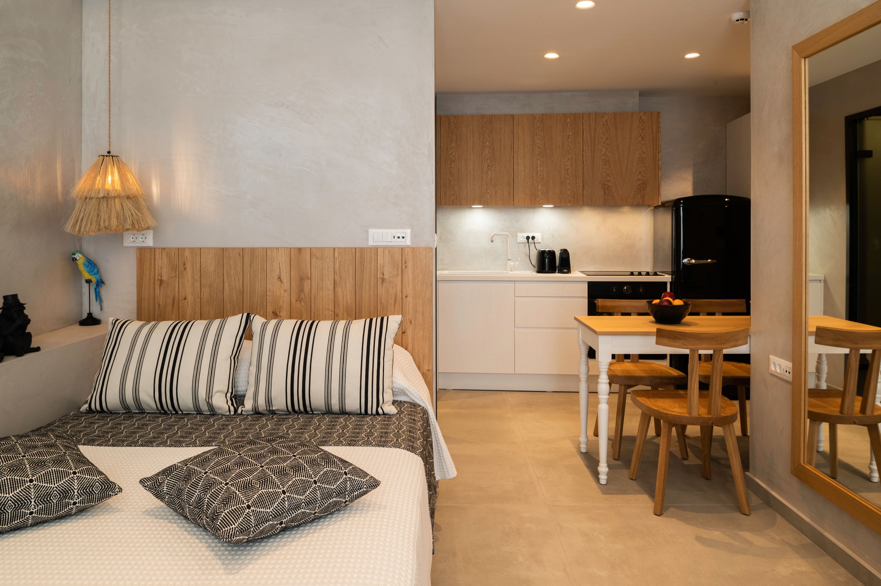 Habitación pequeña con cama, mesita de noche y kitchenette.