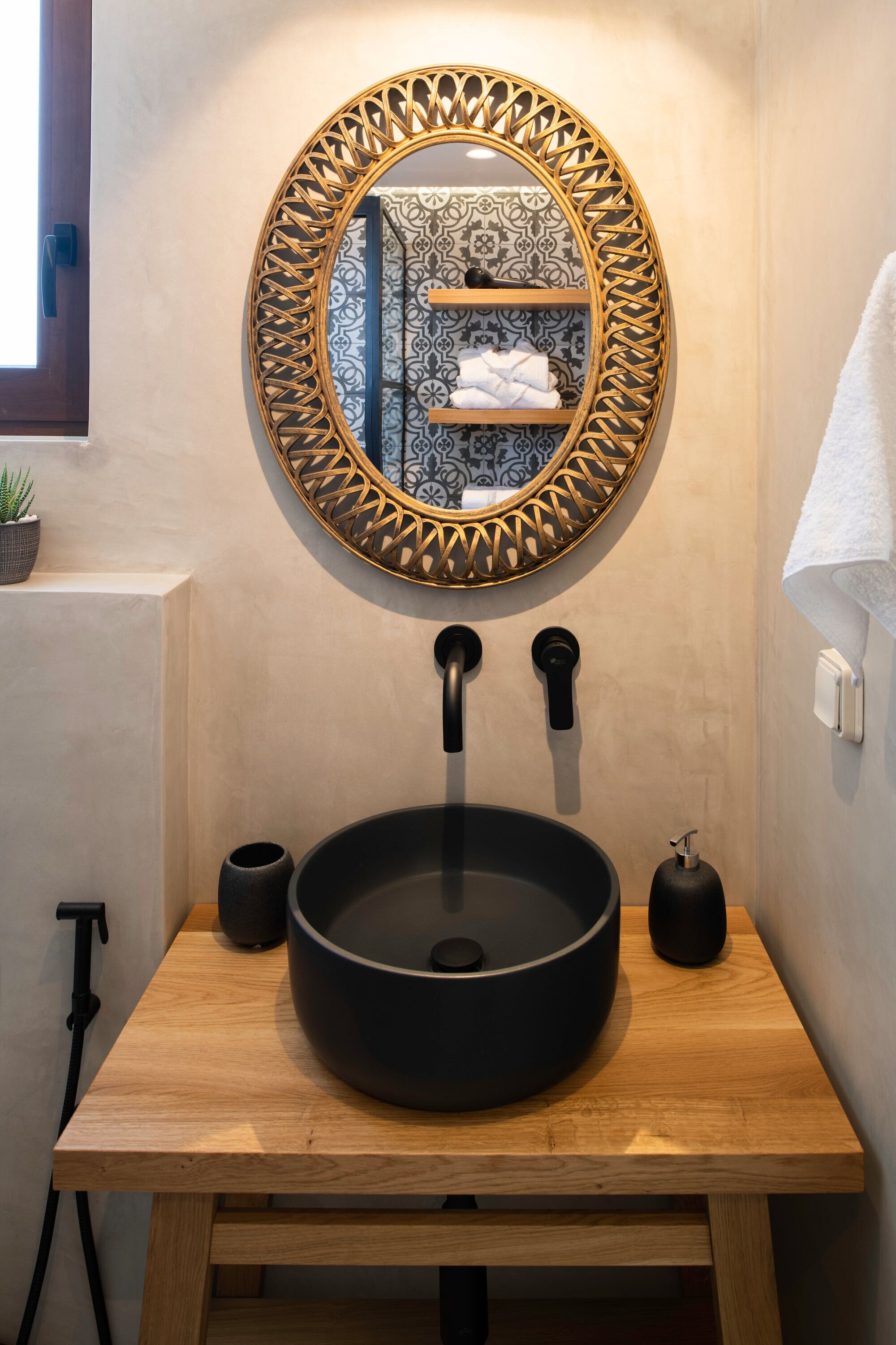 Un baño con espejo redondo, lavamanos negro y tocador de madera.