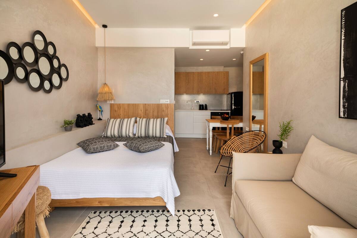 A modern bedroom with a bed, bedside table, and a view into a kitchen area.