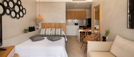 A modern bedroom with a bed, bedside table, and a view into a kitchen area.