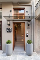 Entrada de un hotel con puerta de vidrio, un cartel que dice 'Petalo Suites' y dos macetas grandes.