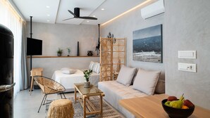 A modern living room with a sofa, coffee table, and a TV. There is a decorative screen, a painting, and a fruit bowl on the table. - Petalo Suites (Rethymno)