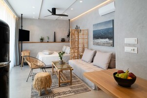 Una sala de estar moderna con un sofá, una mesa de centro y un televisor. Hay un separador decorativo, un cuadro y un frutero sobre la mesa.