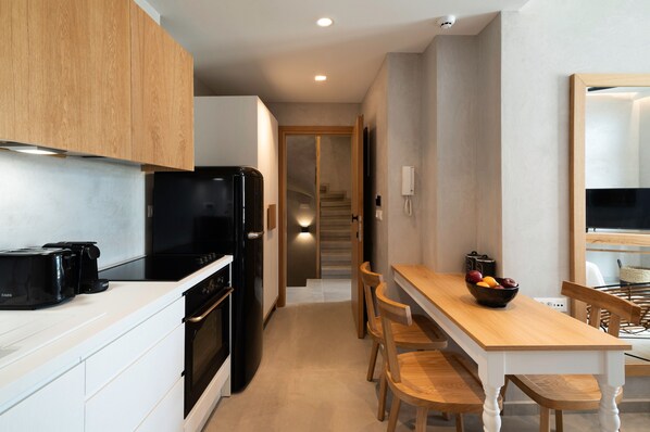 A modern kitchen with white cabinetry, a black refrigerator, a stove, and a dining area with a wooden table and chairs.