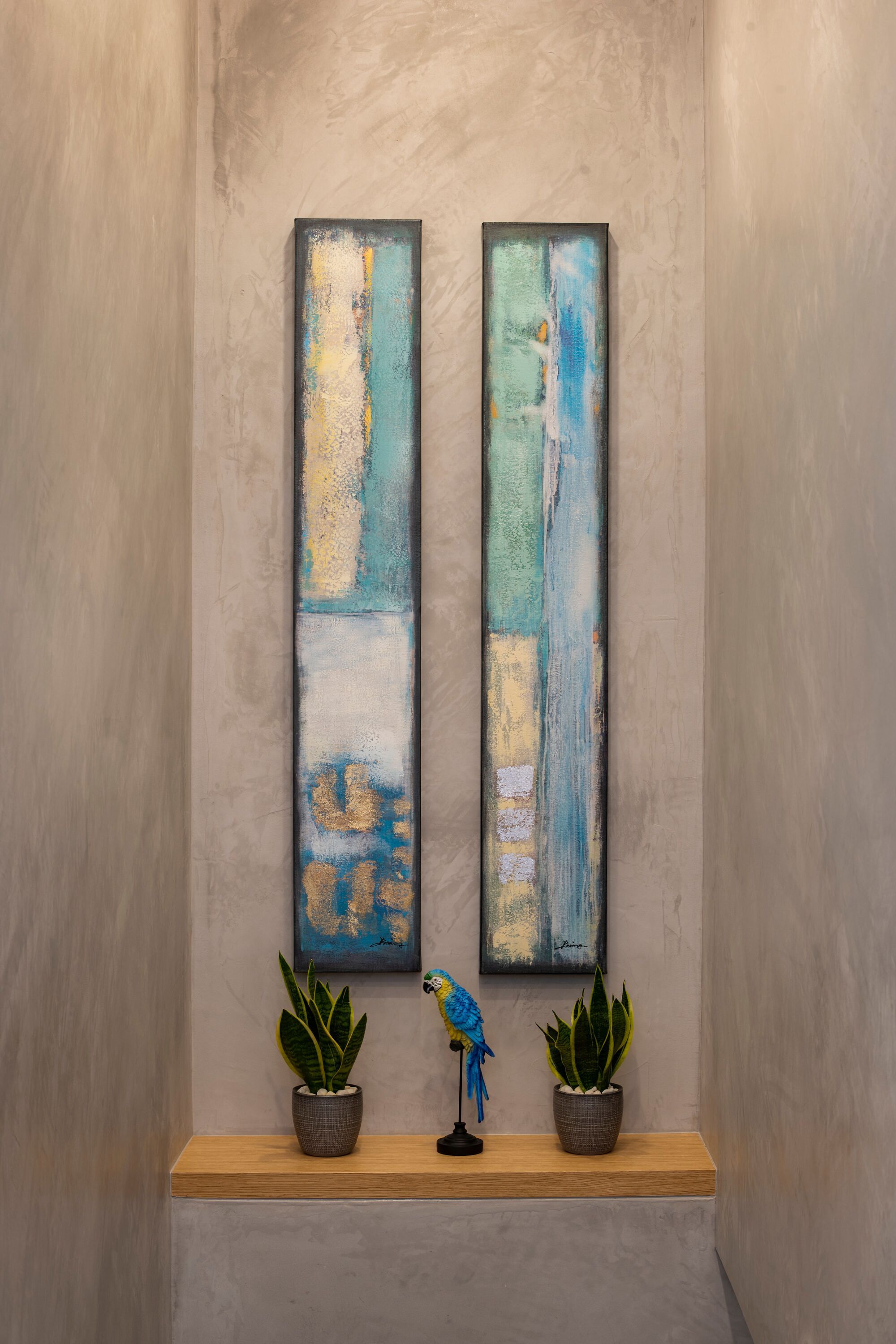 A hallway with two abstract paintings on the wall, a wooden bench with potted plants, and a parrot figurine.
