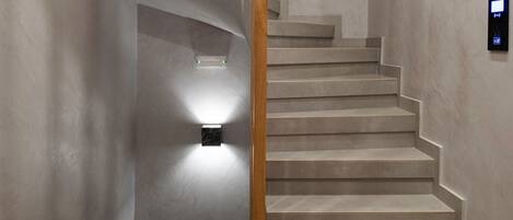 A staircase with a wooden handrail, a wall-mounted light fixture, and a small black object on the wall.