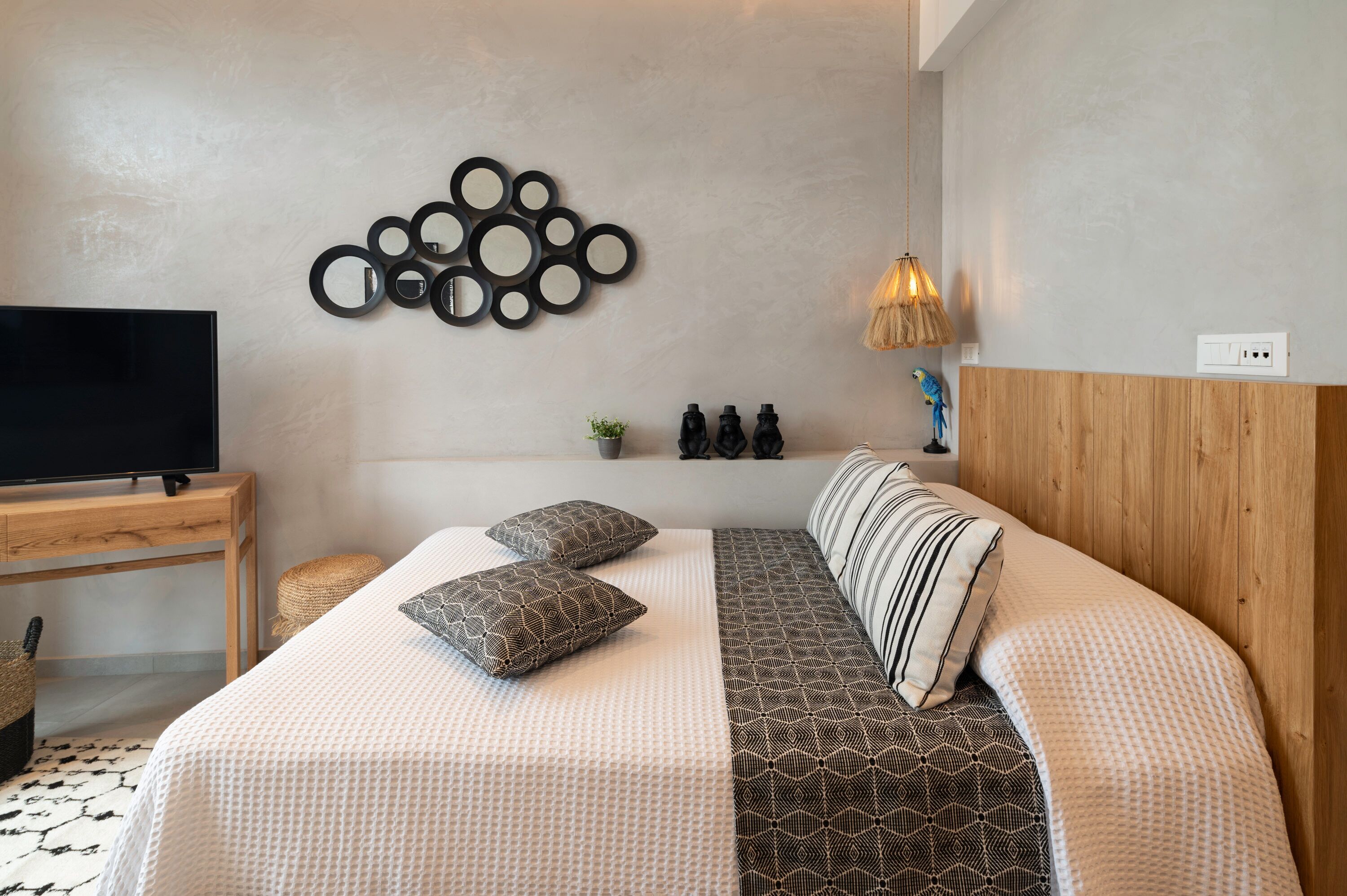 Un dormitorio ordenado con cama, almohadas, televisor, una obra de arte en la pared y una lámpara.