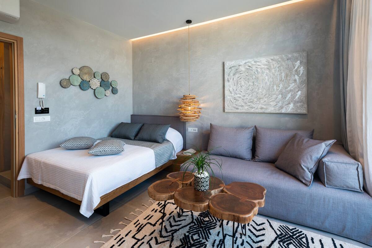 A modern bedroom with a bed, a sofa, a hanging light fixture, a wall art piece, and a small plant.