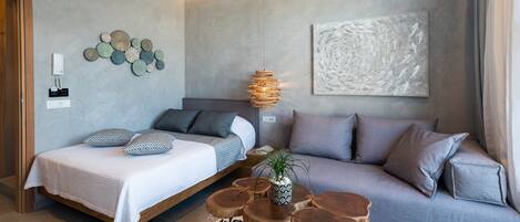 A modern bedroom with a bed, a sofa, a hanging light fixture, a wall art piece, and a small plant.