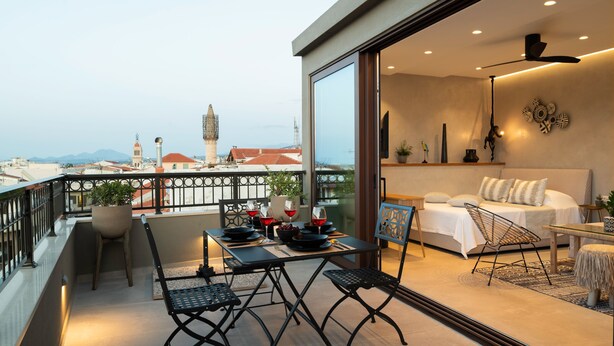 A balcony with a dining table, chairs, and a view of the cityscape. - Petalo Suites (Rethymno)