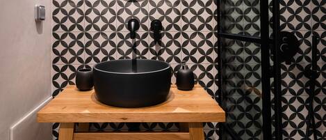 Un baño con un lavabo negro sobre un mueble de madera, un espejo redondo y una pared con estampado geométrico.