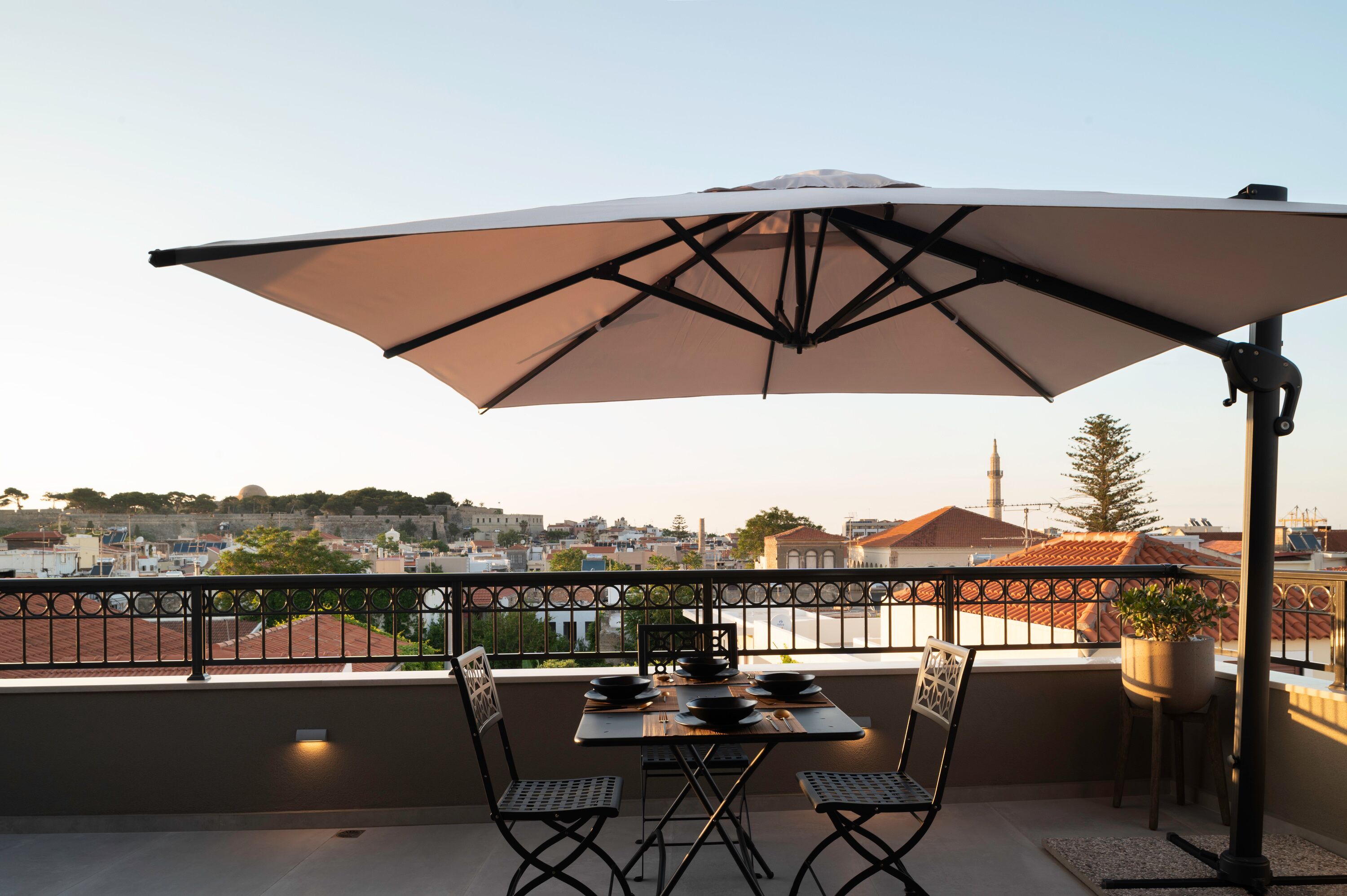 A balcony with a table set for two, a large umbrella, and a view of the cityscape.