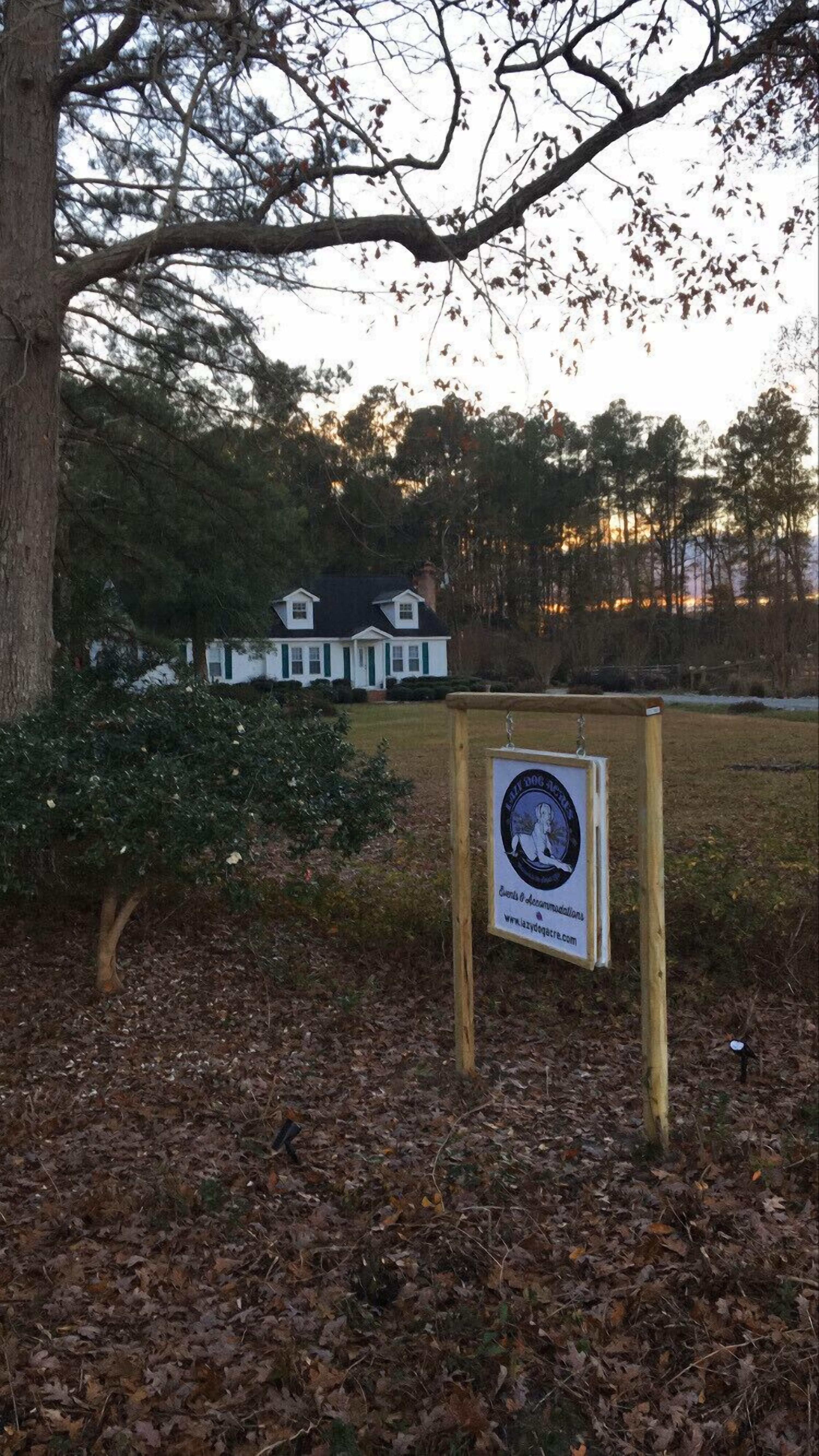 A signboard with a logo and text, a tree, and a building in the background.