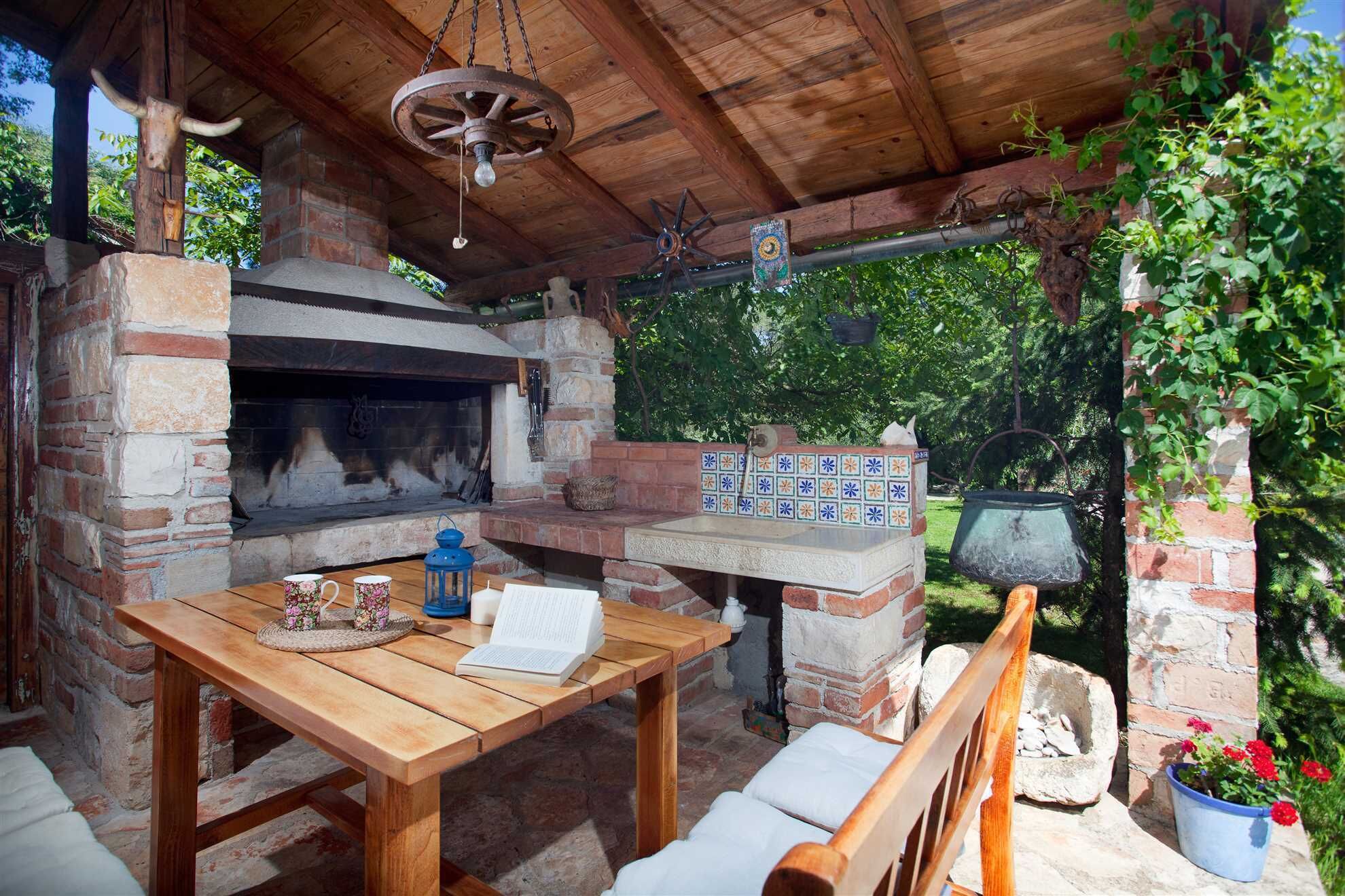 Un four en briques installé à l’extérieur, avec une table et des chaises, le tout entouré de verdure.