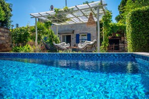 A pool with two wicker chairs and a table, a stone building with a glass roof, and lush greenery. - Casa Oliva (Umag)