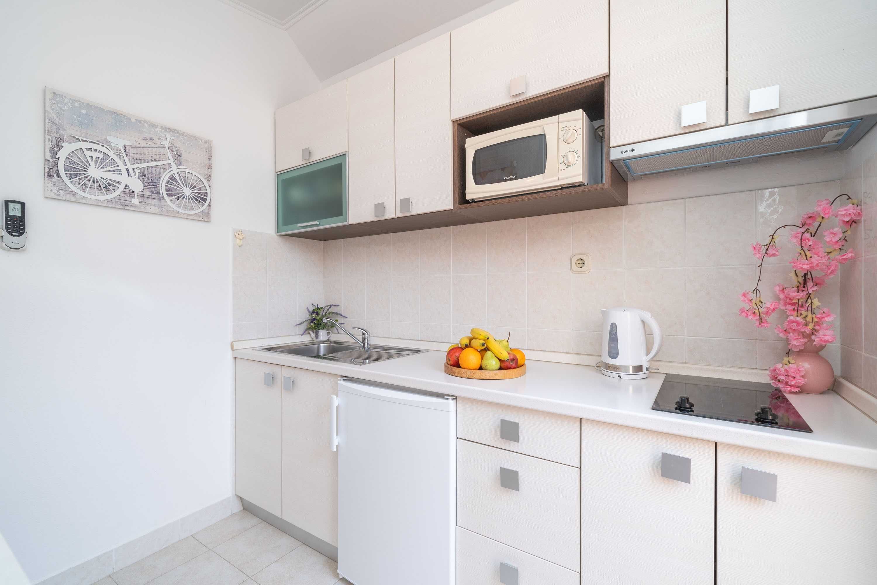 A modern kitchen with white cabinets, a microwave, a sink, and a small refrigerator.