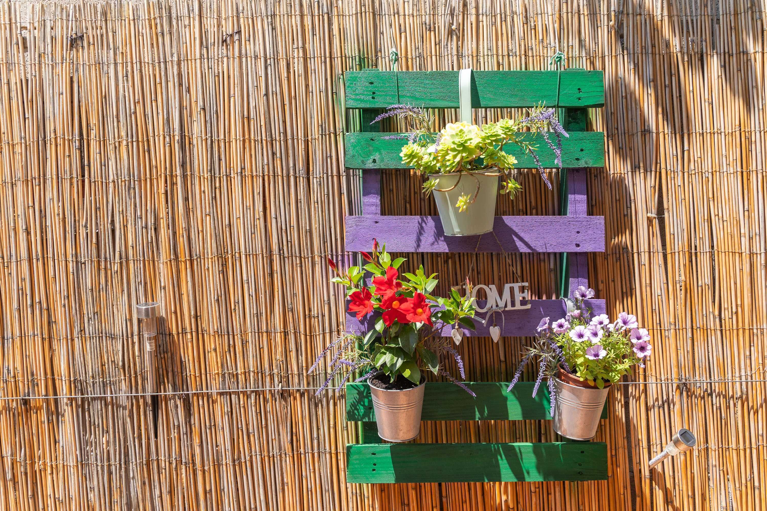 A bamboo fence with a wooden bench and two metal pots with flowers.