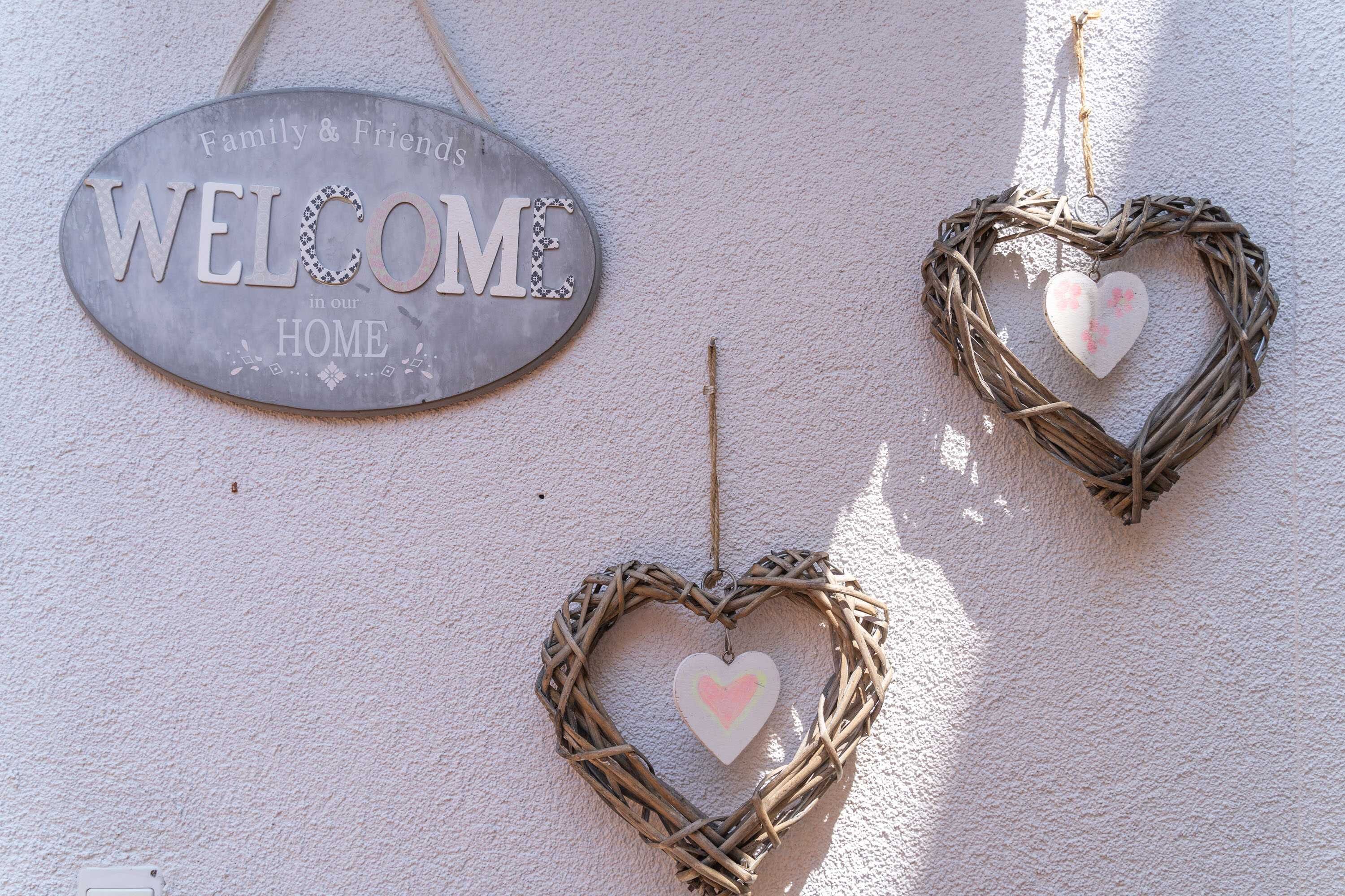 Un letrero de bienvenida y tres decoraciones con forma de corazón en una pared texturizada.