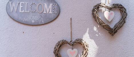 Un letrero de bienvenida y tres decoraciones con forma de corazón en una pared texturizada.