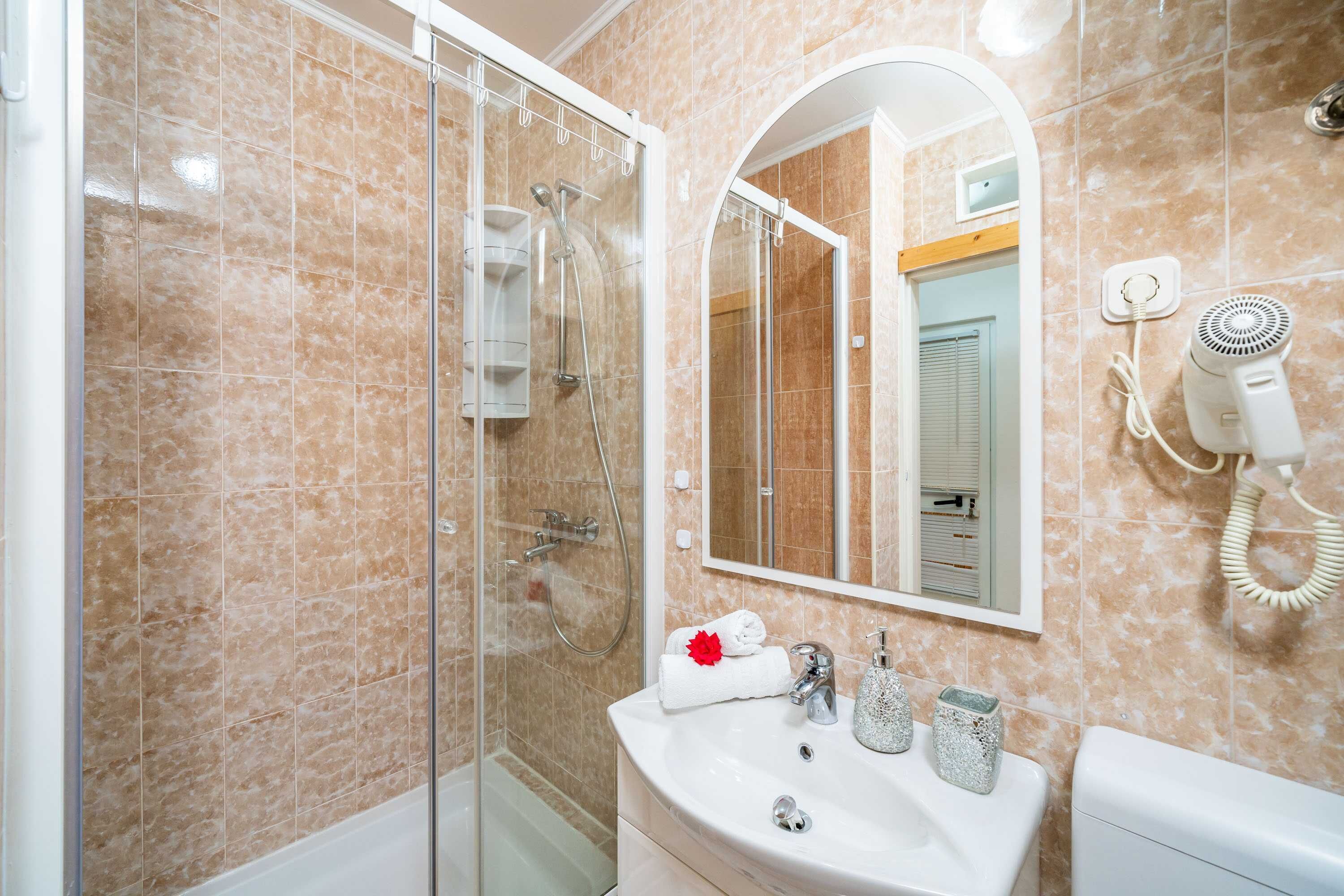 A bathroom with a glass-enclosed shower, a white sink with a mirror above it, and a hairdryer on the wall.