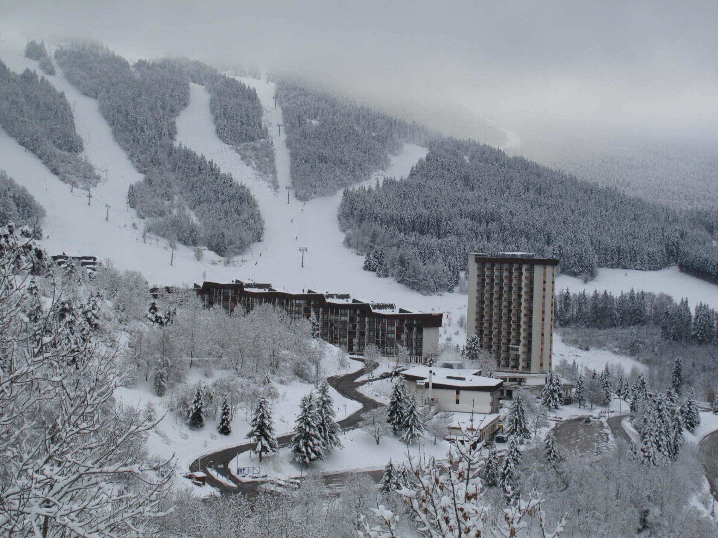 A snow-covered ski resort with a large building, ski lifts, and a winding road.