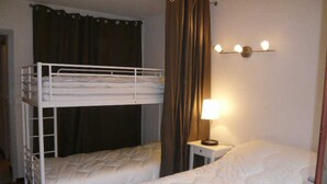 A room with bunk beds, a bedside table with a lamp, and a curtain.