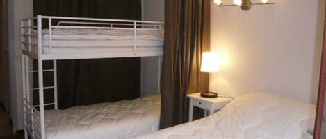 A room with bunk beds, a bedside table with a lamp, and a curtain.
