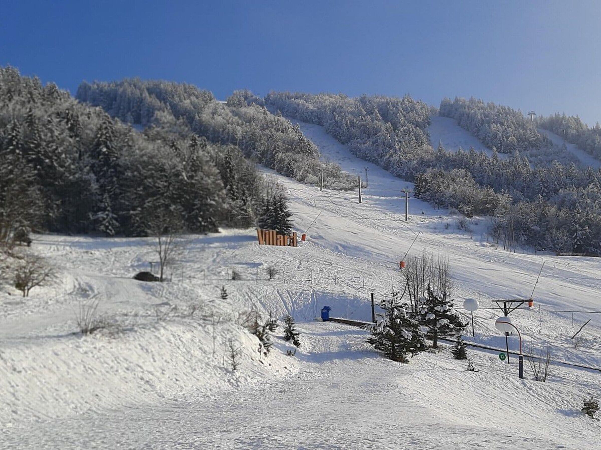 Une piste de ski enneigée avec une structure en bois portant l'inscription « Villard » et des installations de télésiège.