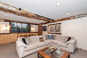 Una sala de estar acogedora con un sofá modular, vigas de madera en el techo y grandes ventanales con vistas al exterior.