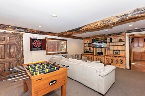 A room with a foosball table, a dartboard, a sofa, and wooden cabinets. - Falling Leaves by Destination Big Bear : Premiere Moonridge Cabin Offering a Perfect Setting for Escaping to the Mountains! (Big Bear Lake)