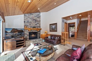 Una sala de estar con chimenea de piedra, televisor y una escalera que sube a otro nivel.