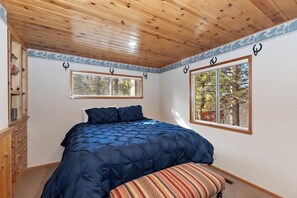 Un dormitorio con una cama grande, dos ventanas, techo de madera y un aparador.